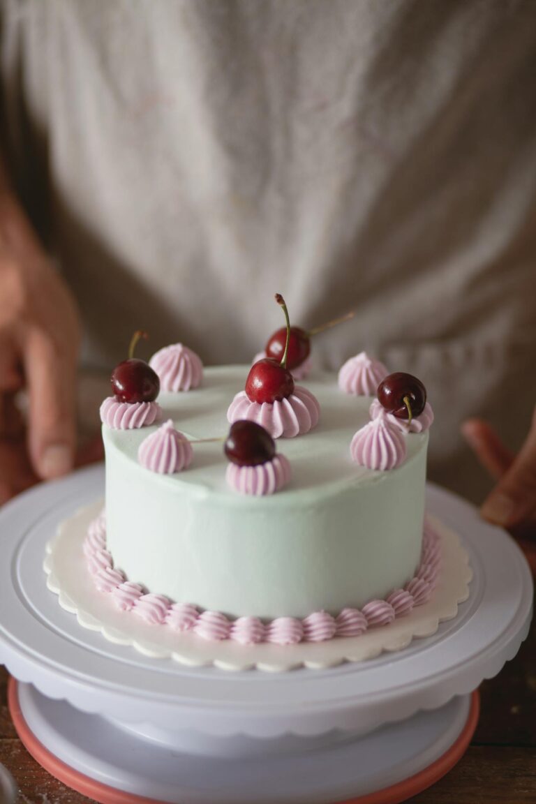 A delicious cake topped with cherries and pastel whipped cream, perfect for celebrations.