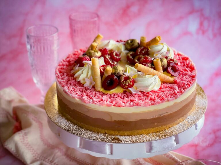 A vibrant triple layered cheesecake topped with fresh berries and chocolate curls.