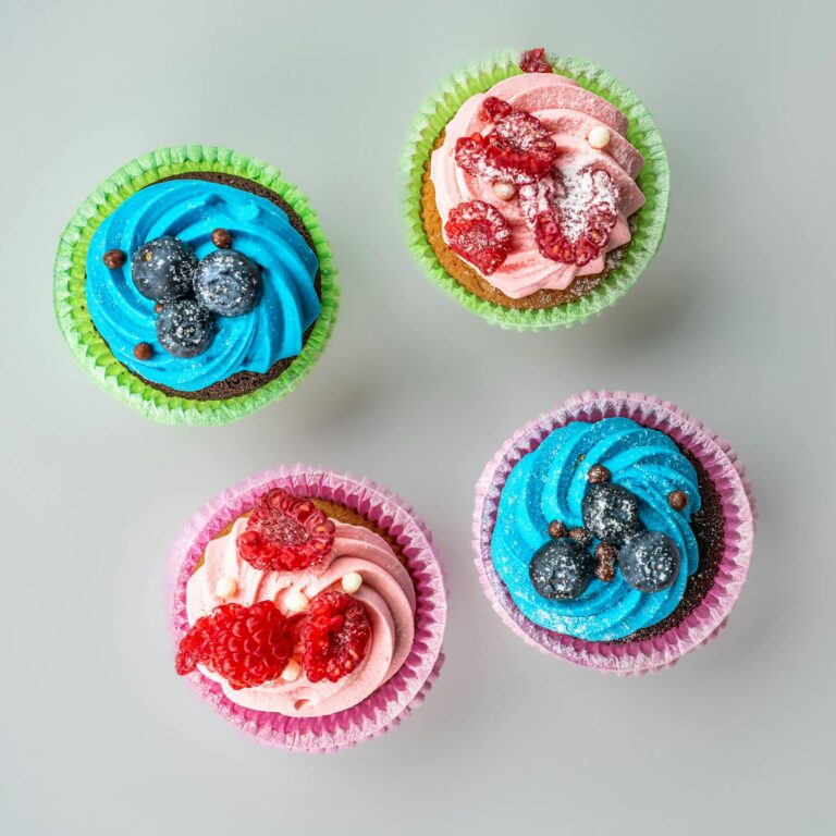 Brightly colored cupcakes topped with raspberries and blueberries viewed from above.