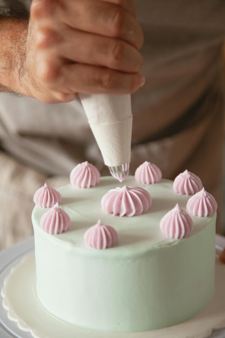 Hand decorating a cake with pink icing in a detailed close-up shot.