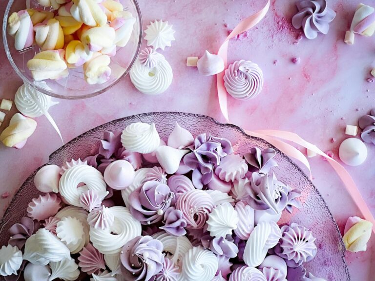 Vibrant pink and purple meringues with marshmallows on a decorative platter.